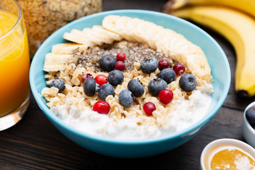 Healthy fitness breakfast: oatmeal with bananas, blueberries and cranberries, chia seeds and yogurt on dark wooden board with texture