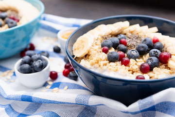Healthy fitness breakfast: oatmeal with bananas, blueberries and cranberries, chia seeds and yogurt on blue and white towel