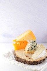 Different cheeses, pears and peanuts on wooden stand. Hard yellow cheese and camembert on white napkin. Dairy products and fruits for breakfast. Healthy food. Copy space