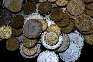 Ukrainian coins with one euro coin isolated on black background. Close-up view. Coins are located at the upper side of frame. A conceptual image.