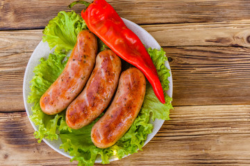 Ceramic plate with grilled sausages, pepper and lettuce leaves on wooden table. Top view