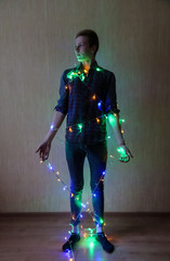 A young guy wrapped in a multi-colored Christmas garland