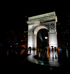 lighted washington park arch with silhouettes of people in the rain