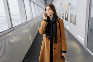 Businesswoman on airport talking on the smartphone while walking with hand luggage in train station or airpot going to boarding gate. Girl using mobile phone for conversation.