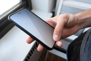 young man's hand holding a smart phone inside home near a window