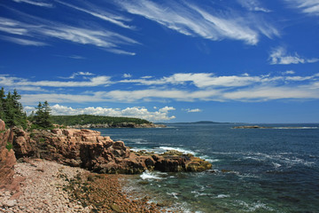 The rugged coast of Acadia National Park, Maine, under wispy clouds on a sunny summer day.