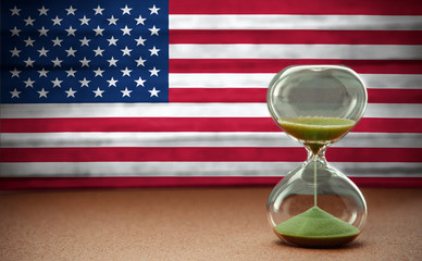 Sand running through the bulbs of an hourglass measuring the passing time in a countdown to a...