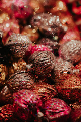Brown, red and orange walnut shaped Christmas tree ornaments in warm tones with sparkling glitter and out of focus, blurry bokeh background