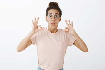 Better thank ok. Portrait of impressed and surprised enthusiastic charismatic nerdy female in round glasses showing okay gestures with orbs folding lips in excitement, liking awesome perfomance