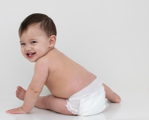 Baby wear white diaper sit aside and turn his face with smile  in white background 