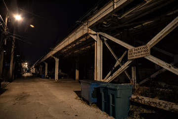 Dark and scary downtown urban city street alley under an eerie vintage industrial railroad subway bridge at night