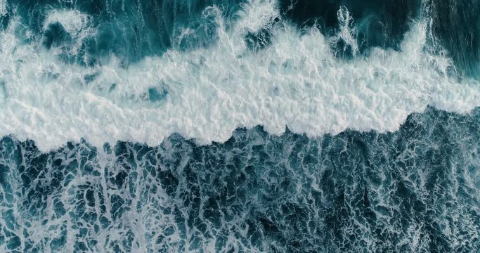 Aerial headover drone footage of huge waves crashing on dark sand of the coast 4K