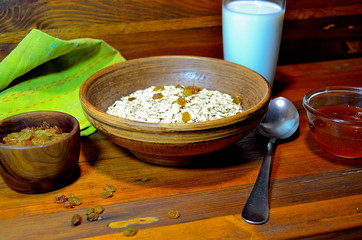 Porridge in a ceramic plate, milk, honey, raisins on a wooden background.