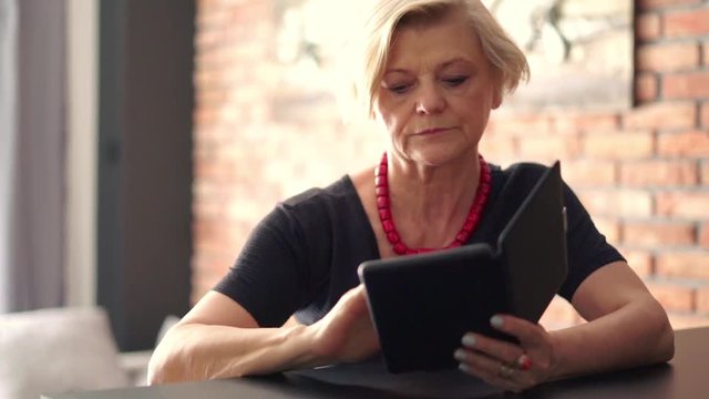 Beautiful, senior woman reading something on e-book at home
