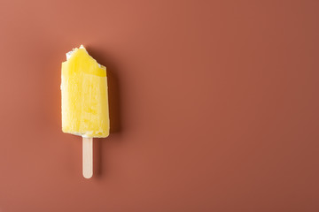 yellow popsicle with some bites on a chocolate brown background