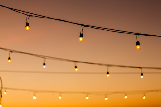 vintage light bulbs on string wire against sunset decor in outdoors wedding event party