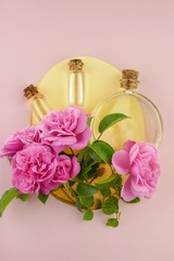 rose essential oil set in glass bottles and large pink roses on a combination pink and yellow background in pastel  tones