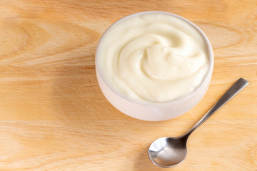 Bowl of yogurt and spoon on the wood table. Yogurt made from milk fermented by added bacteria, often sweetened and flavored.