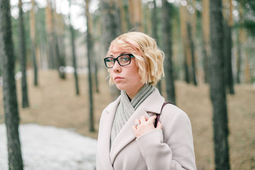 Cute girl in big glasses and white coat outdoors in the park
