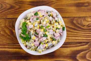 Tasty salad with sausage, green pea, canned corn, bell pepper, cucumber and mayonnaise on wooden table. Top view
