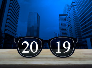 2019 white text with black eye glasses on wooden table over modern office city tower and skyscraper, Business vision happy new year 2019 concept