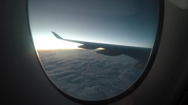 Airplane flying above clouds at sunset, view of wing from plane window.