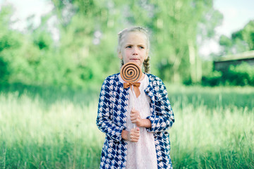 Little girl with pigtails and a big lollipop on a green summer background