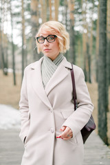 Beautiful blonde girl with glasses and a white coat for a walk in the park