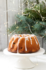 Pie with raisins and icing from powdered sugar on the background of fir branches and garlands. Rustic style.