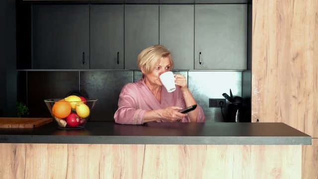 Beautiful senior woman watching TV in the kitchen
