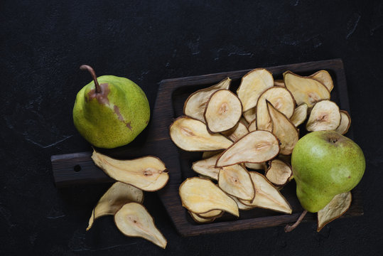 Wooden serving tray with crispy fruit chips made of pear, flatlay on a black stone background, horizontal shot