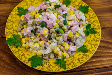 Tasty salad with sausage, green pea, canned corn, bell pepper, cucumber and mayonnaise on wooden table