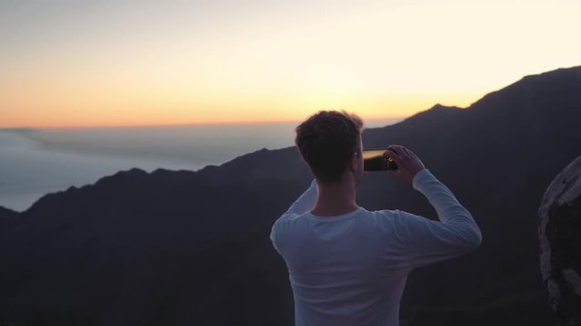 high in the mountains on the coast of the island in the ocean a guy takes pictures using a smartphone