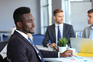 Smiling confident African businessman in a meeting with a colleagues seated at a conference table...