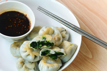 fried garlic chives dim sum or garlic steamed chives dumplings with spicy soy sauce in white plate with chopsticks on wood background