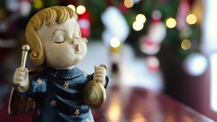 Little terracotta angel with the background of a Christmas tree with lights out of focus