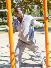 Fototapeta premium Young male training different exercises at chin-up bar in park outdoor