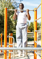 Obraz premium Active african american man doing workout at pull-up bar in park