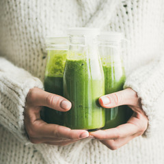 Winter seasonal smoothie drink detox. Female in light knitted sweater holding bottles of green...