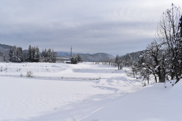 Fototapeta na wymiar 晴れた日の雪原と工場と山々