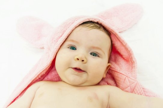Cute newborn three months old baby girl after bath in a funny pink towel with bunny ears.