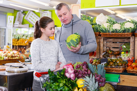 Tweenage girl with her father buying cauliflower in supermarket