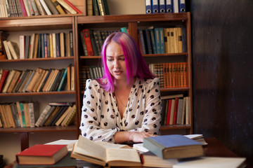 beautiful woman with pink hair reads books in the library