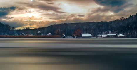 Obraz premium Winter panorama with windmills, the sun through the clouds, and motion blur on lake