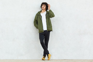 Photo of attractive curly man with thoughtful expression, scratches head, dressed in fashionable clothes, poses against white studio wall, feels lonely thinks about something. People and style concept © sementsova321