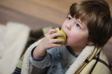 Portrait of a small curly-haired boy. A child wrapped in a rug eats an apple. A two-year-old boy hides under a blanket.