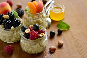 Oat flakes with various berries, hazelnuts and honey in glass jars, copy space