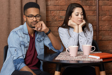 Young mixed race couple have quarrel in cafeteria, displeased facial expression, sort out...