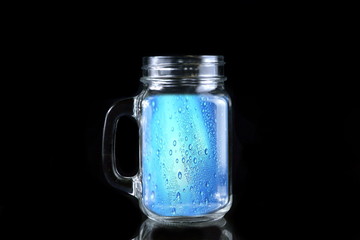 blue water with drops on the glass in a transparent bottle on a black background
