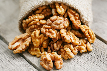 Walnuts in a burlap bag on a wooden gray background.